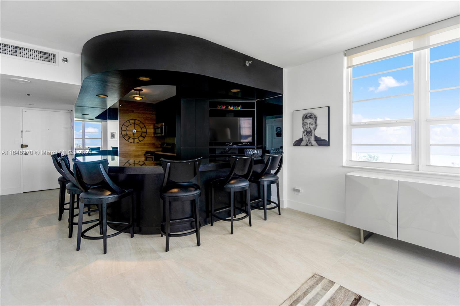 A modern kitchen features a curved black bar, bar stools, and a large wall clock — 100 Lincoln Rd # 548, Miami Beach FL 33139, MIAMI BEACH, FL