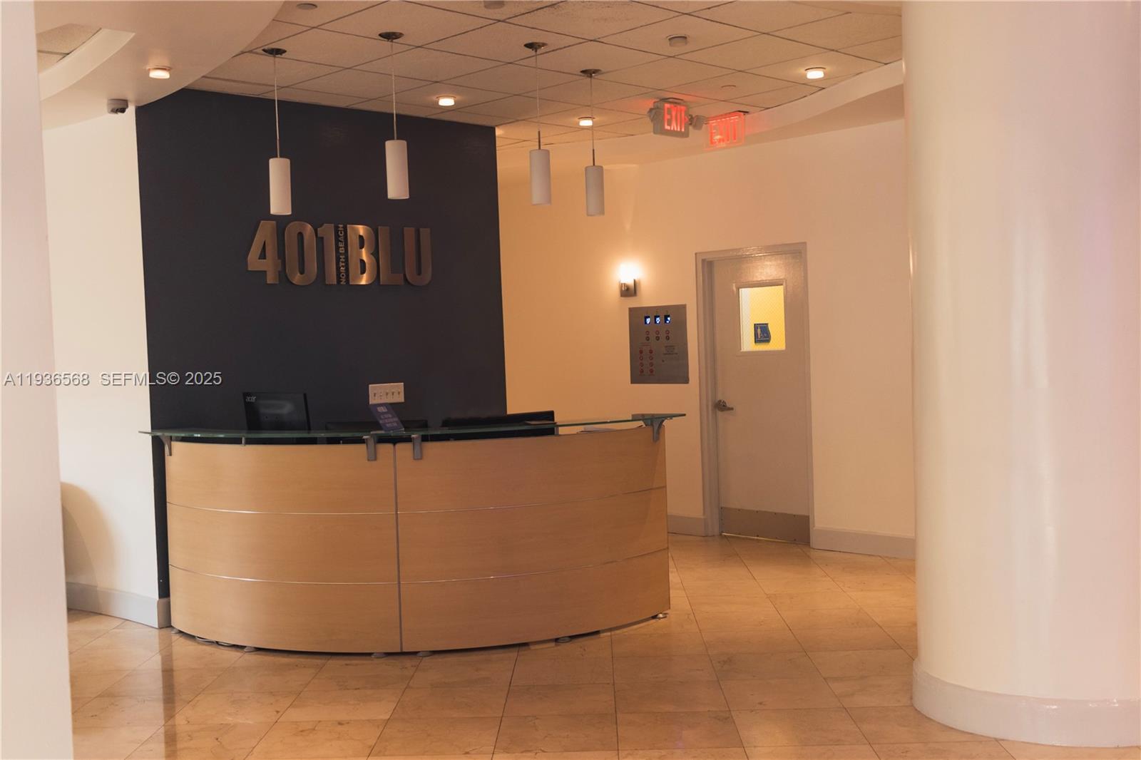 A reception area features a curved wooden desk in front of a dark accent wall — 401 69th St # 304, Miami Beach FL 33141, MIAMI BEACH, FL
