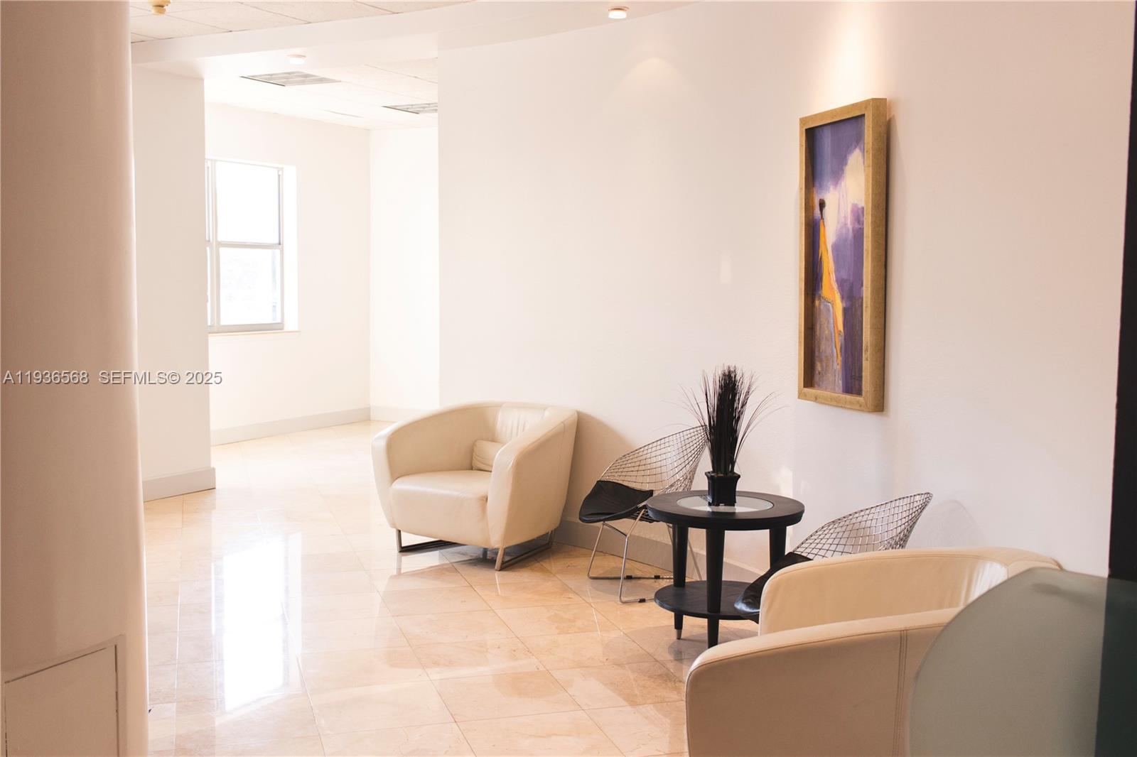 A waiting area features cream-colored armchairs, wire-frame chairs, a small round table, and wall art — 401 69th St # 304, Miami Beach FL 33141, MIAMI BEACH, FL