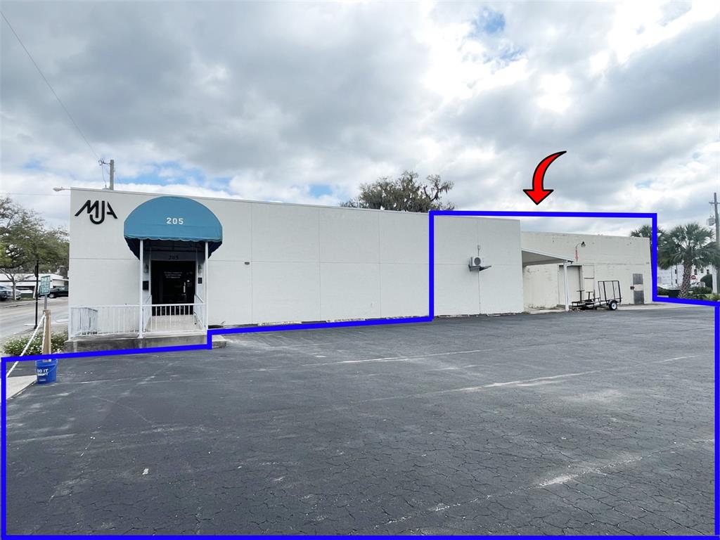 A white commercial building features a blue awning, a parking lot, and a loading area — 205 S MAGNOLIA AVENUE, OCALA, FL