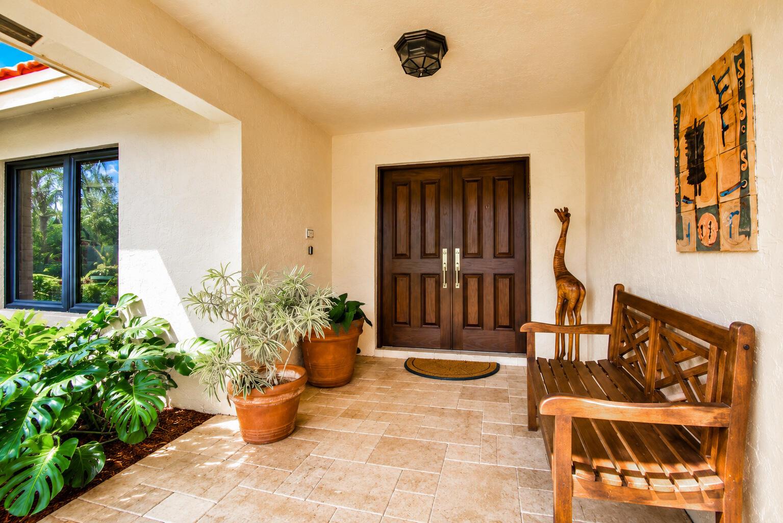 A covered entryway features a double wooden door, a wooden bench, and potted plants — 7838 Tennyson Court, Boca Raton FL 33433, BOCA RATON, FL