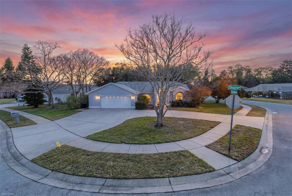 A single-story house with a two-car garage sits on a corner lot at sunset — 3138 ELLINGTON WAY, NEW PORT RICHEY, FL