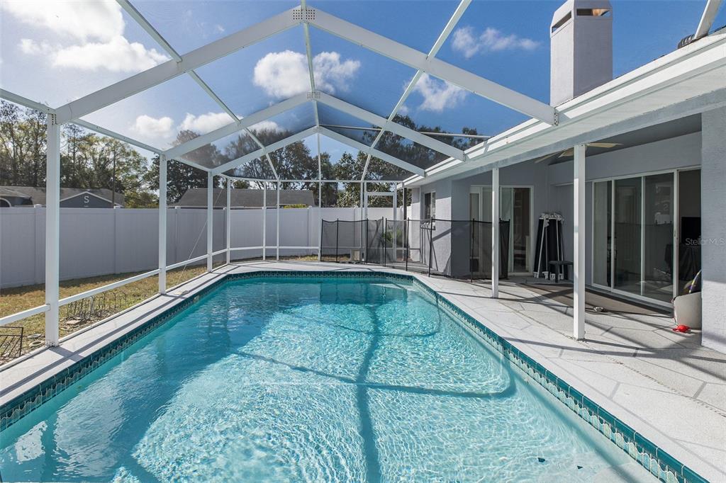A swimming pool with a screened enclosure sits on a patio next to a house — 3138 ELLINGTON WAY, NEW PORT RICHEY, FL