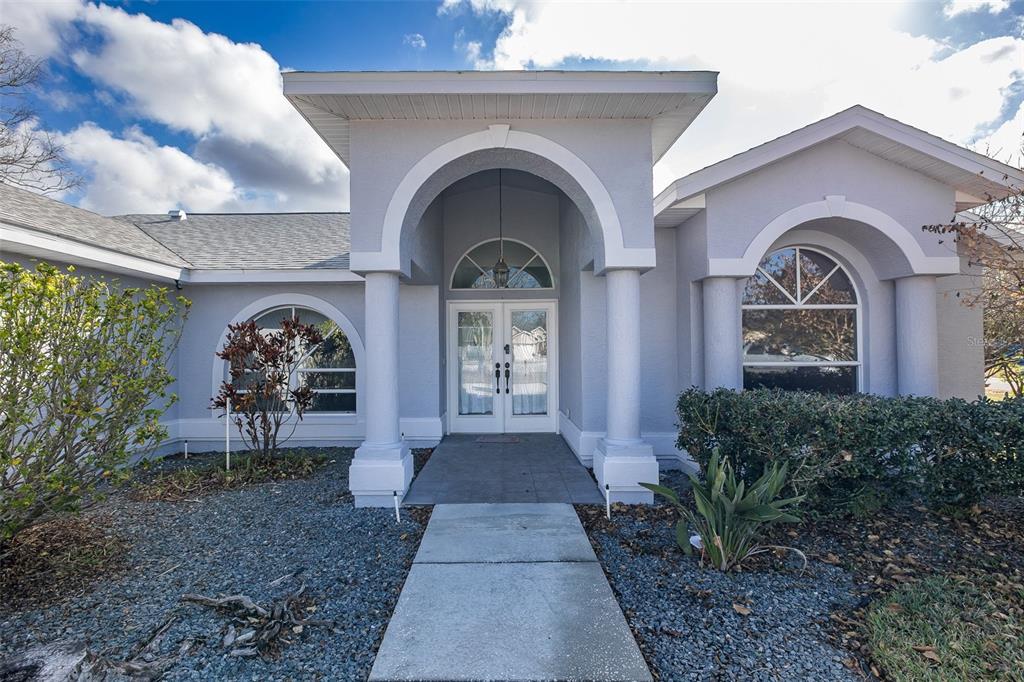 The exterior of a gray house features a covered entryway with columns and arched windows — 3138 ELLINGTON WAY, NEW PORT RICHEY, FL