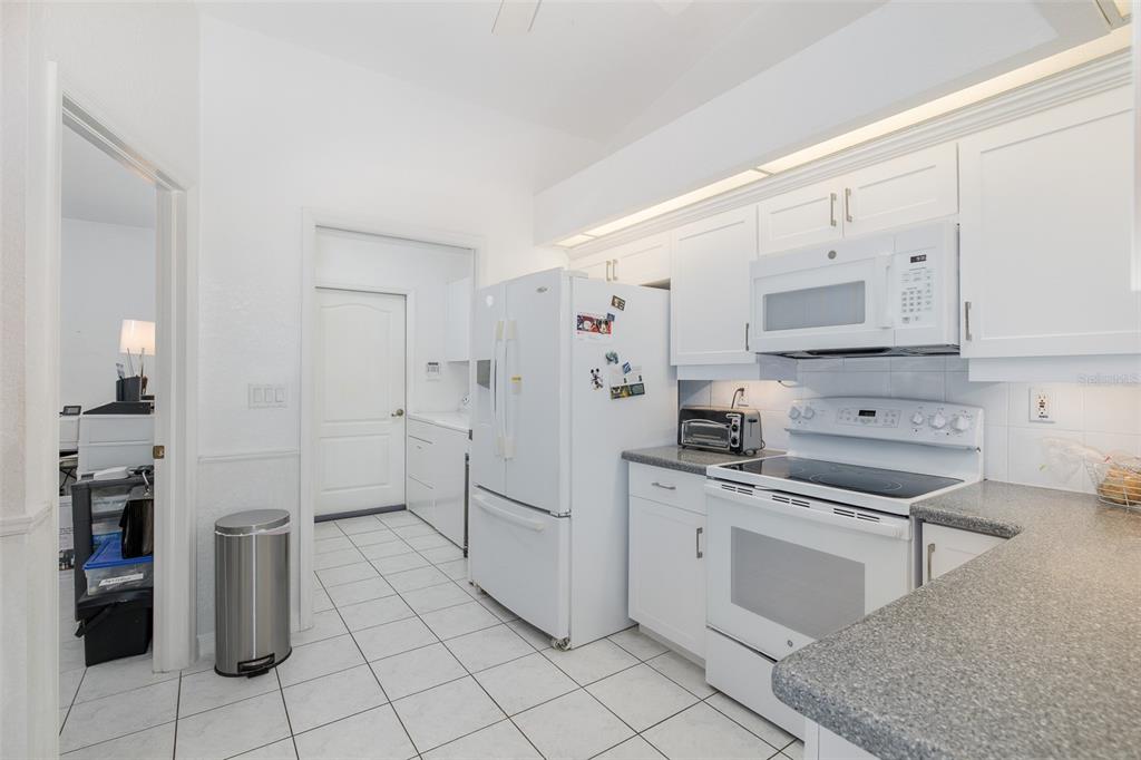 A white kitchen with tile flooring, white cabinets, a refrigerator, and a freestanding electric range — 3138 ELLINGTON WAY, NEW PORT RICHEY, FL