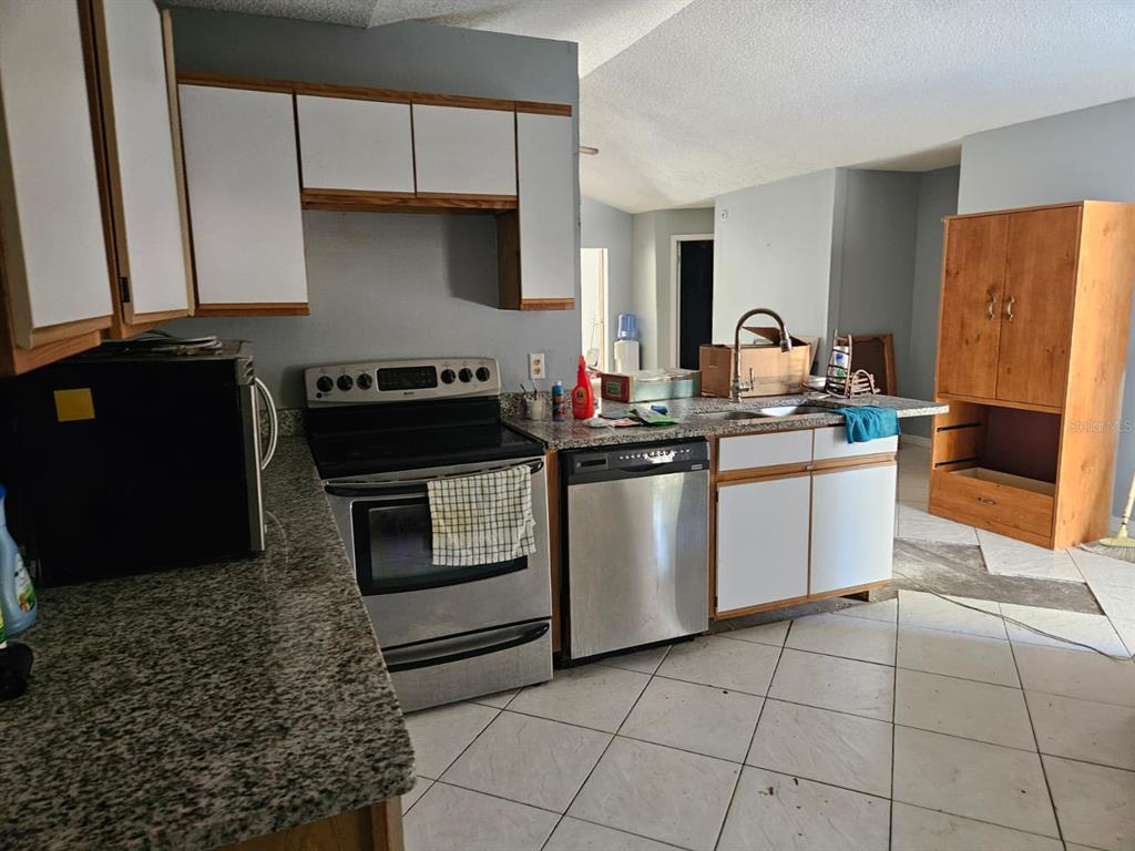 A kitchen features white cabinets, granite countertops, stainless steel appliances, and light-colored tile flooring — 1821 17TH STREET, ST CLOUD, FL