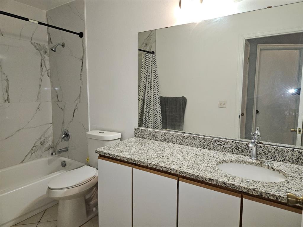 A bathroom features a granite vanity, white cabinets, and a tub with marble-look tile — 1821 17TH STREET, ST CLOUD, FL
