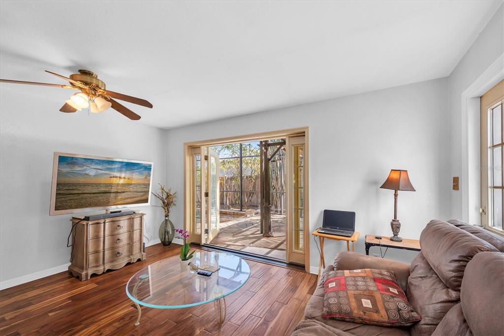 A living room features wood-look tile floors, a ceiling fan, and glass doors to a patio — 1700 74TH AVENUE N, ST PETERSBURG, FL