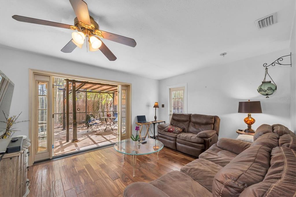 A living room features brown leather furniture, wood-look tile flooring, and sliding doors to a patio — 1700 74TH AVENUE N, ST PETERSBURG, FL