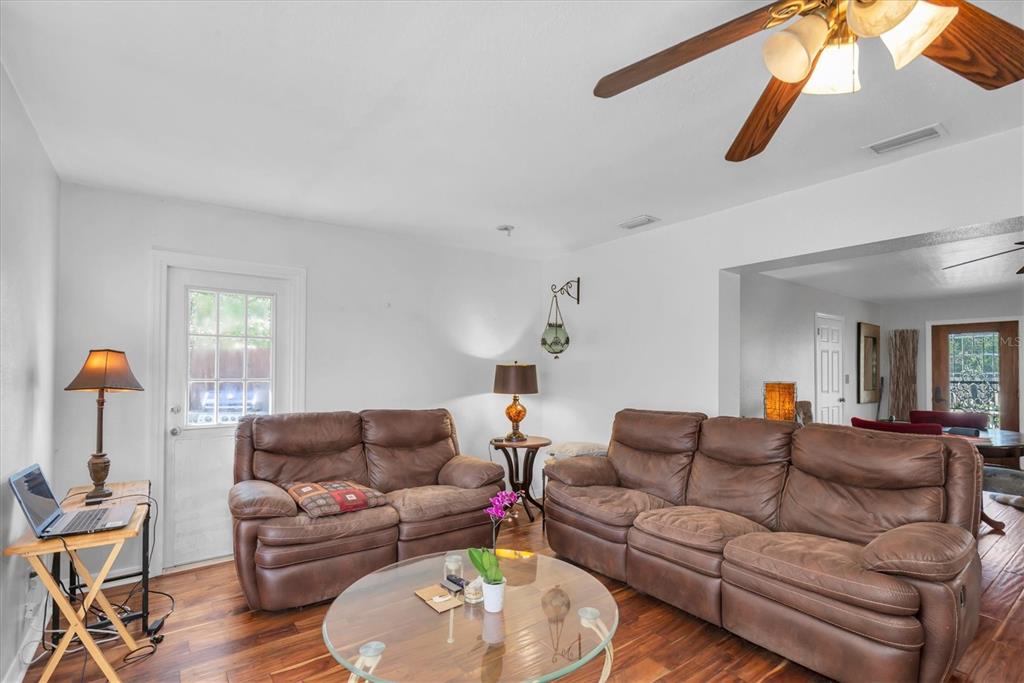 A living room features two brown leather sofas, a glass coffee table, and wood flooring — 1700 74TH AVENUE N, ST PETERSBURG, FL
