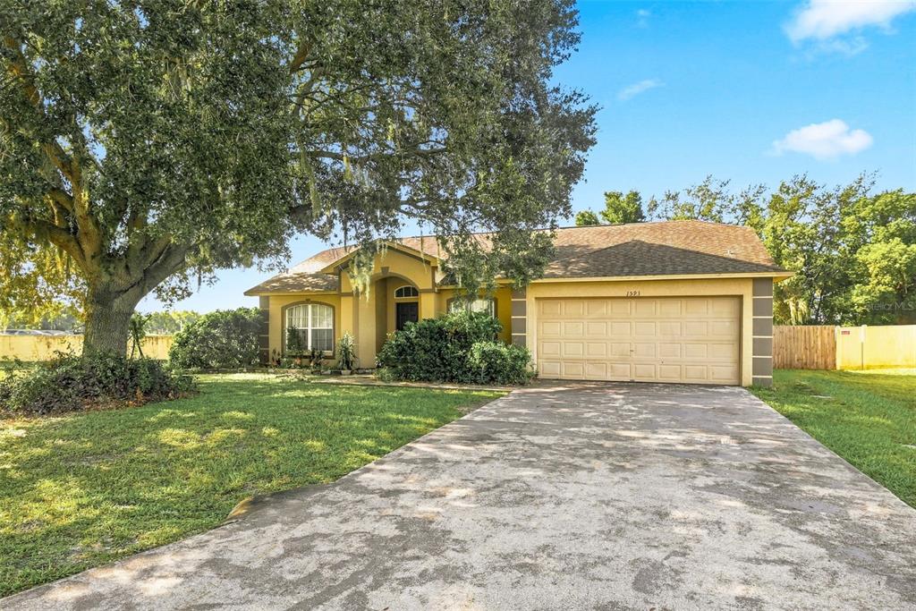 A single-story house with a beige stucco exterior, a two-car garage, and a large tree — 1593 WATSON OAKS COURT, LAKELAND, FL