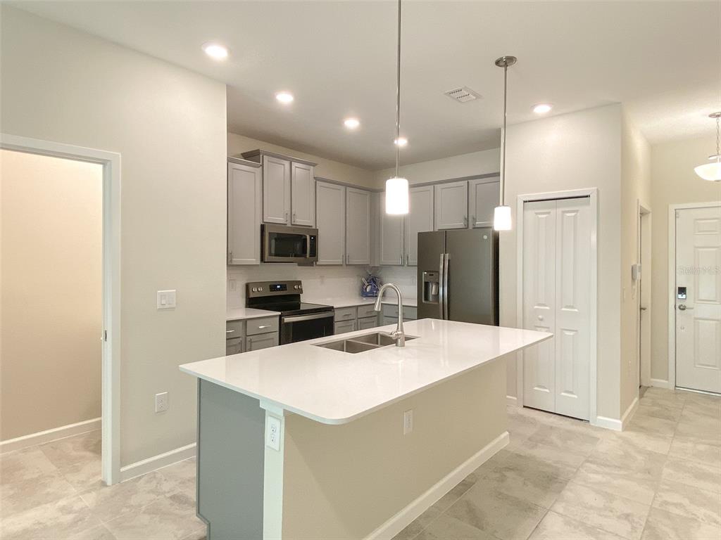 A modern kitchen features a central island, grey cabinetry, stainless steel appliances, and tile flooring — 10010 RED EAGLE DRIVE, ORLANDO, FL