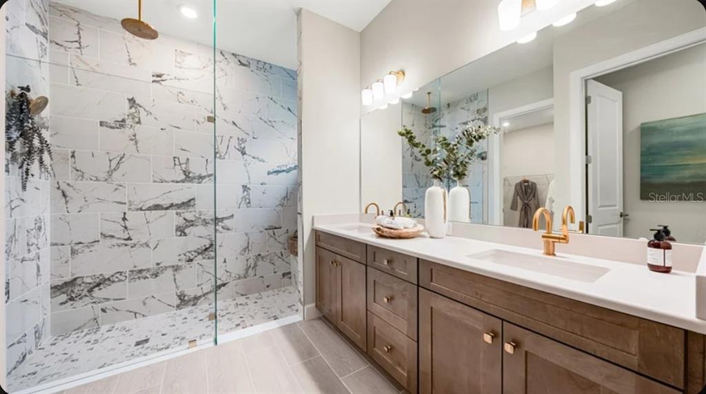 A modern bathroom features a walk-in marble tile shower, double vanity, and gold-toned fixtures — 7652 MOONBEAM AVENUE, SARASOTA, FL