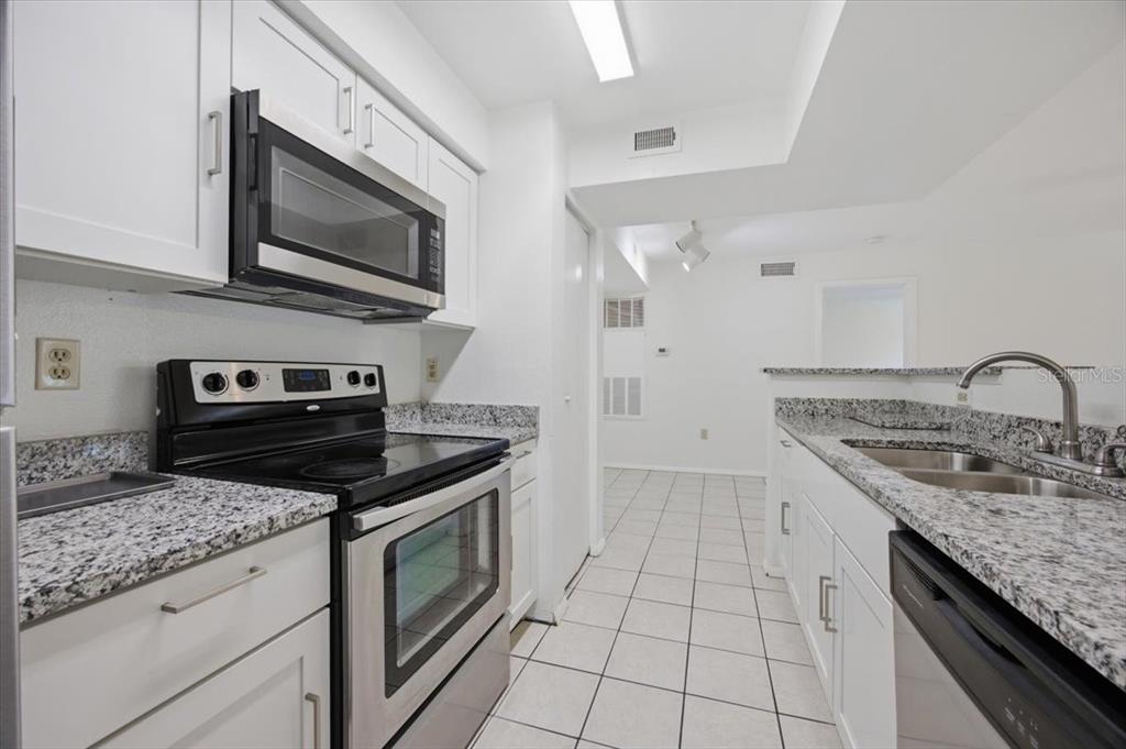 A galley kitchen features white cabinets, granite countertops, and stainless steel appliances — 3032 PARKWAY BOULEVARD UNIT 307, KISSIMMEE, FL