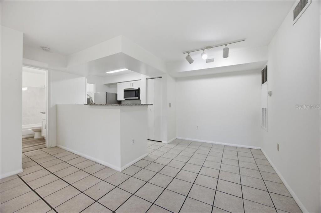 A kitchen with a breakfast bar opens into a tiled dining area with track lighting — 3032 PARKWAY BOULEVARD UNIT 307, KISSIMMEE, FL