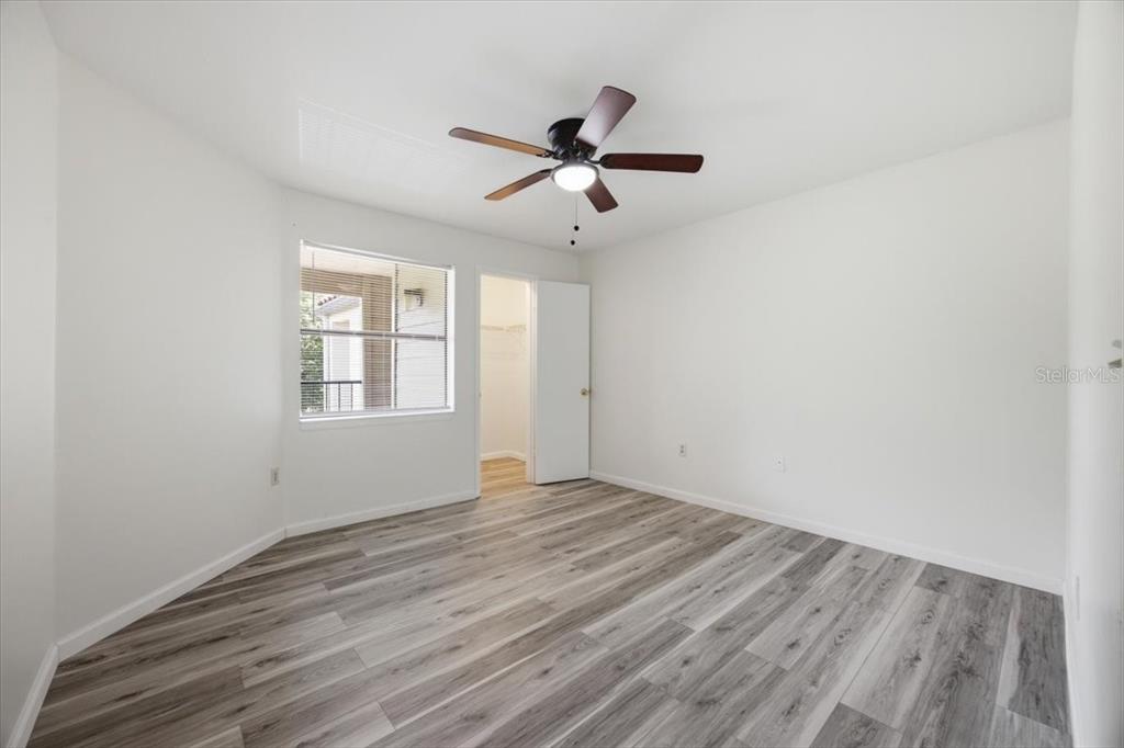 A bedroom features white walls, gray wood-look flooring, a ceiling fan, and a walk-in closet — 3032 PARKWAY BOULEVARD UNIT 307, KISSIMMEE, FL