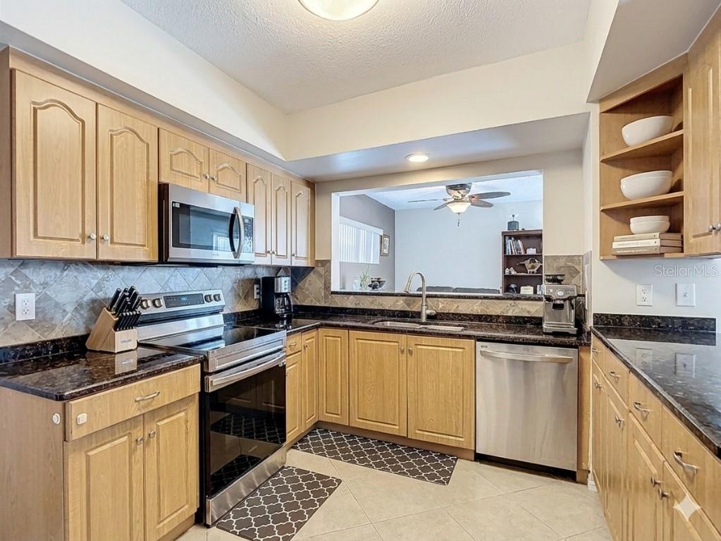 A kitchen features light wood cabinets, dark granite countertops, stainless steel appliances, and tile flooring — 3114 W PARIS STREET, TAMPA, FL