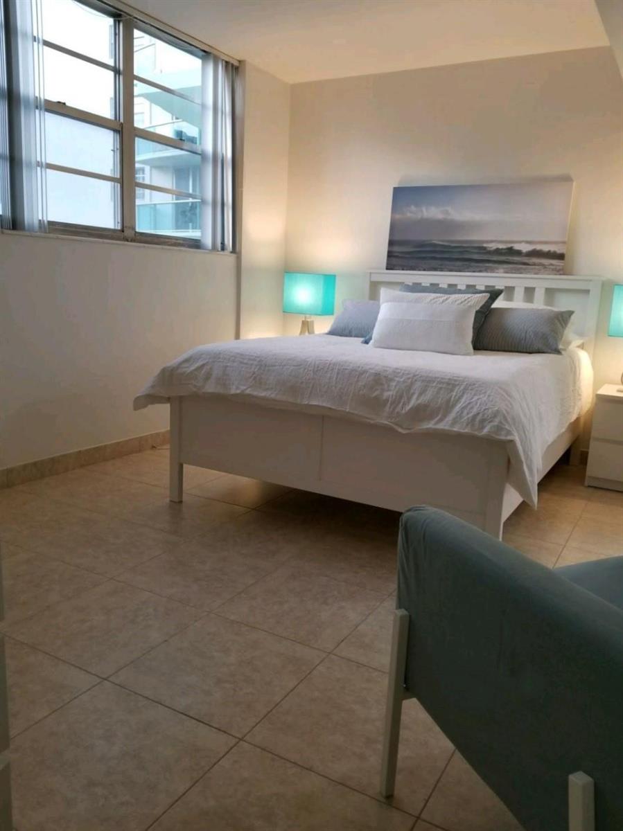 A bedroom features a white bed, blue accent lamps, and tile flooring near a large window — 3801 S Ocean Drive # 7Q, Hollywood FL 33019, HOLLYWOOD, FL