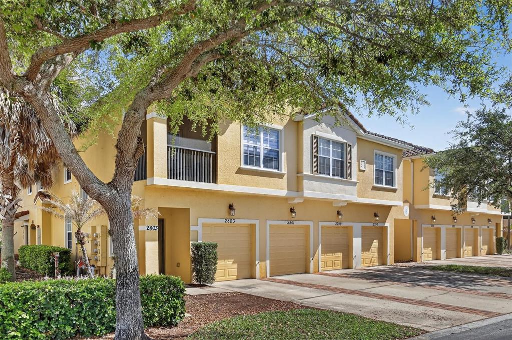 A multi-story yellow townhouse complex with several garage doors and a paved driveway — 2801 OAKWATER DRIVE UNIT 2801, KISSIMMEE, FL