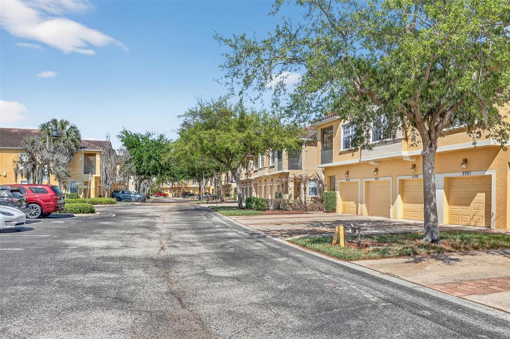 A paved street leads past a row of yellow townhomes with attached garages and trees — 2801 OAKWATER DRIVE UNIT 2801, KISSIMMEE, FL