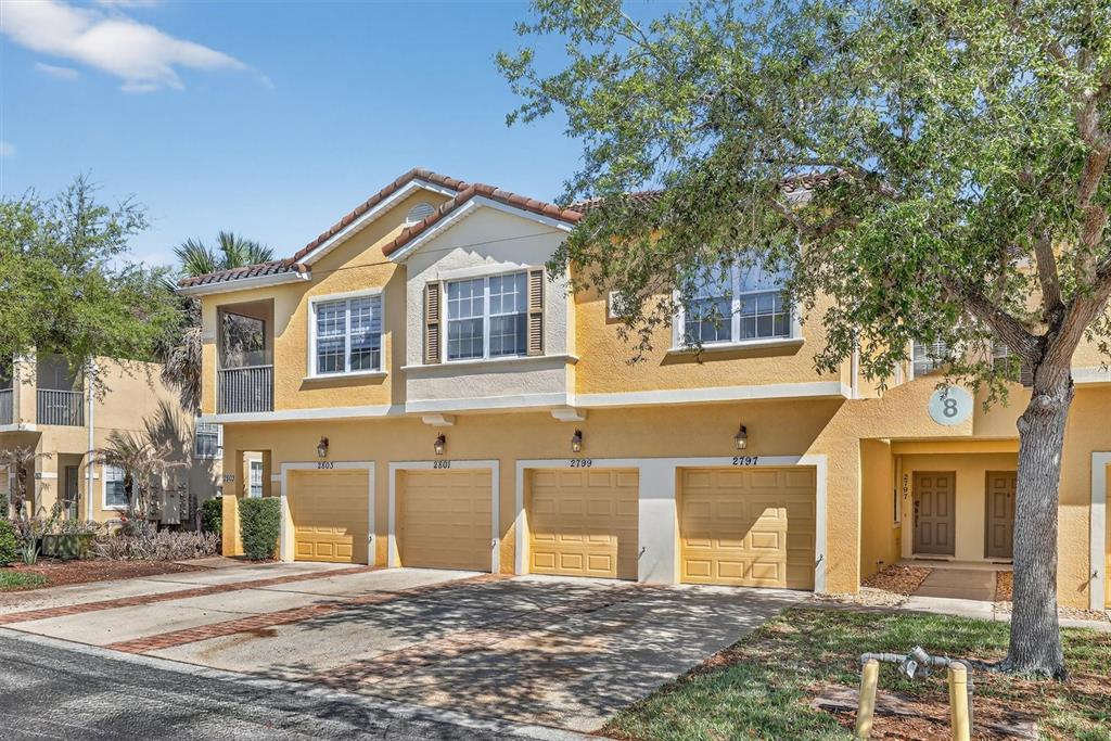 A multi-unit residential building with yellow stucco walls, four garage doors, and a tree — 2801 OAKWATER DRIVE UNIT 2801, KISSIMMEE, FL