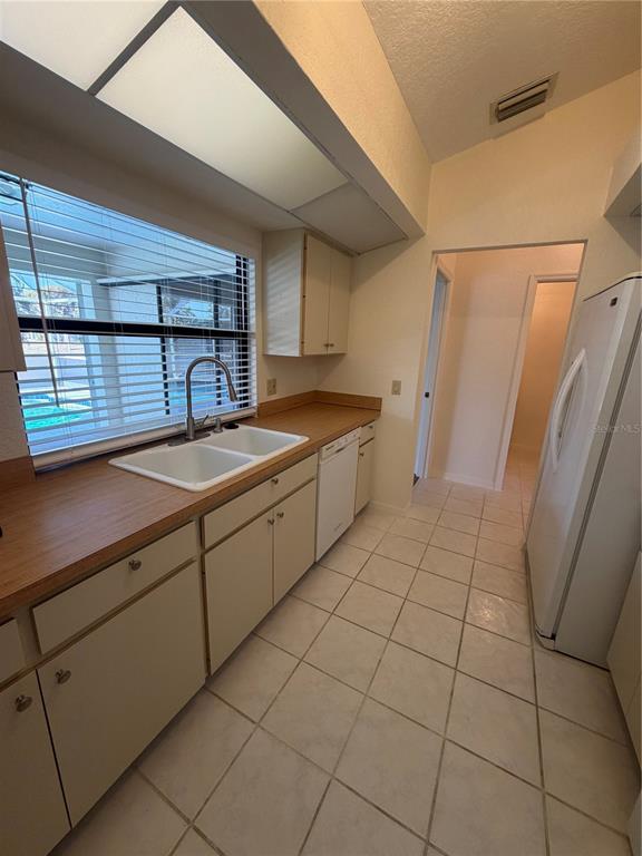 A kitchen with white cabinets, a double sink, wood-look countertops, and white tile flooring — 1612 BLUE LAKE CIRCLE, PUNTA GORDA, FL
