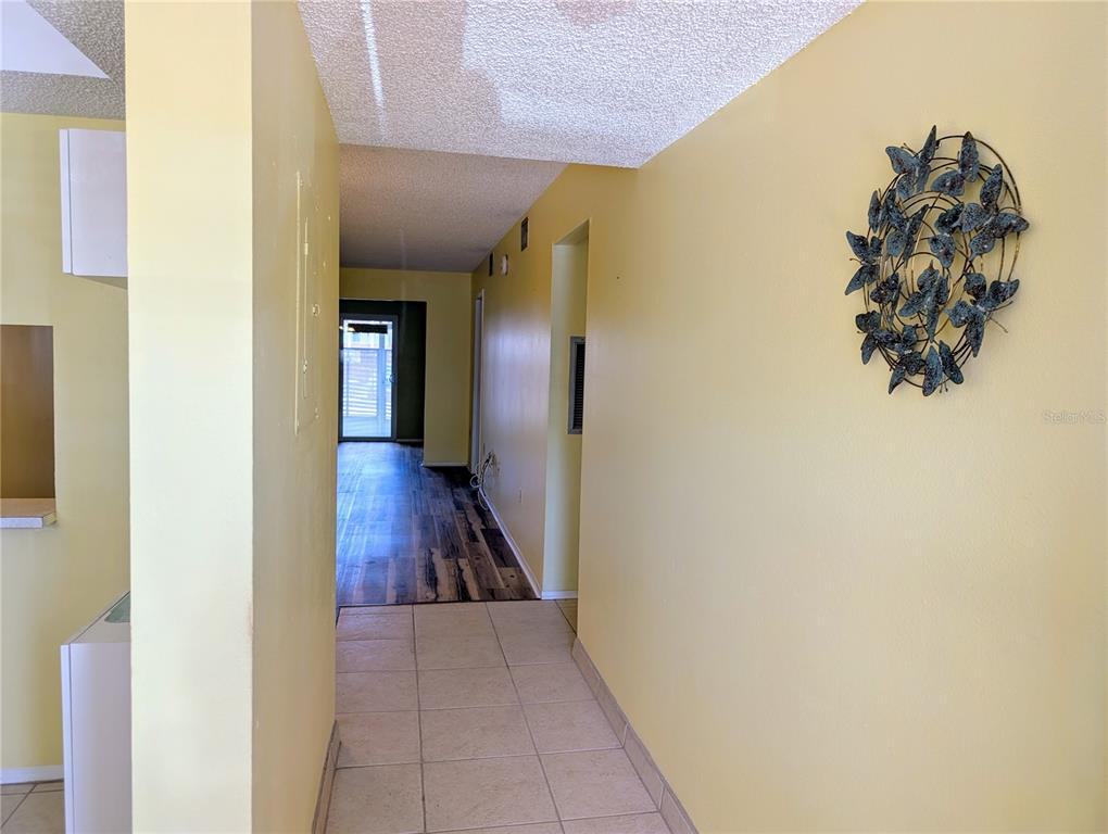 A hallway with tile flooring leads to a room with wood-look floors and a door — 4111 HERON WAY UNIT E-103, BRADENTON, FL