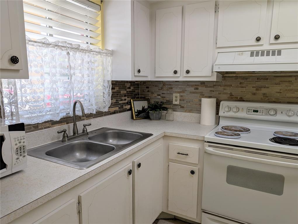 A kitchen features white cabinets, a double-basin sink, a white stove, and a tiled backsplash — 4111 HERON WAY UNIT E-103, BRADENTON, FL