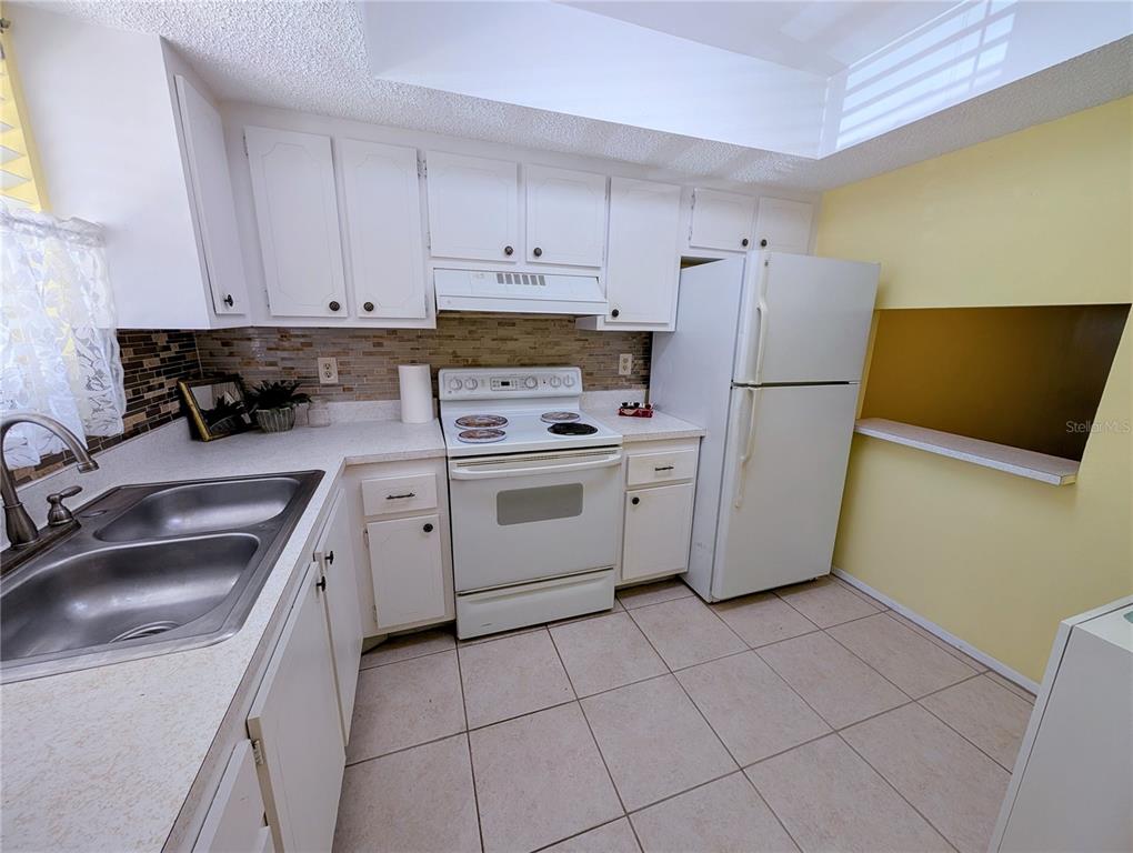 A kitchen features white cabinets, a white stove, a white refrigerator, and tiled flooring — 4111 HERON WAY UNIT E-103, BRADENTON, FL