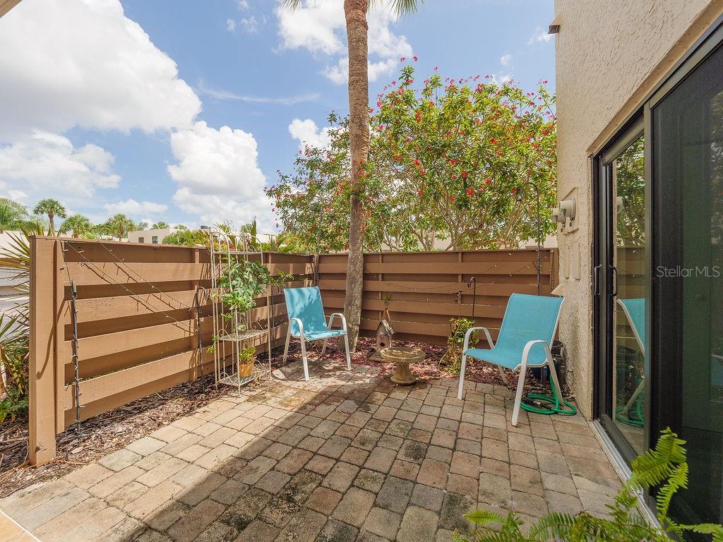 A paved patio features two blue chairs, a small plant stand, and a wooden fence — 193 PINENEEDLE DRIVE, BRADENTON, FL