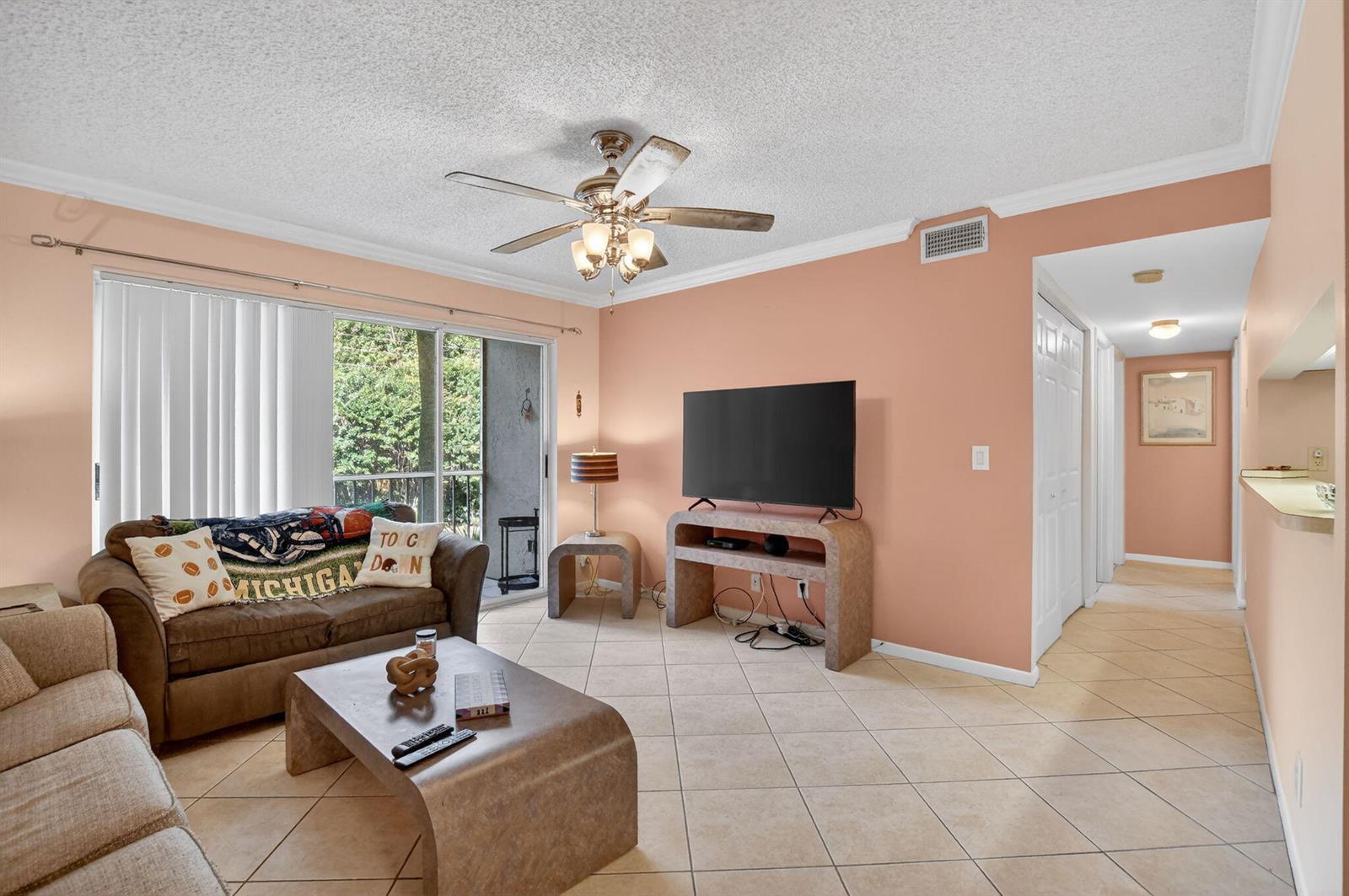 A living room with peach walls, tile flooring, a ceiling fan, and a sliding glass door — 13791 Oneida Drive # C2, Delray Beach FL 33446, DELRAY BEACH, FL