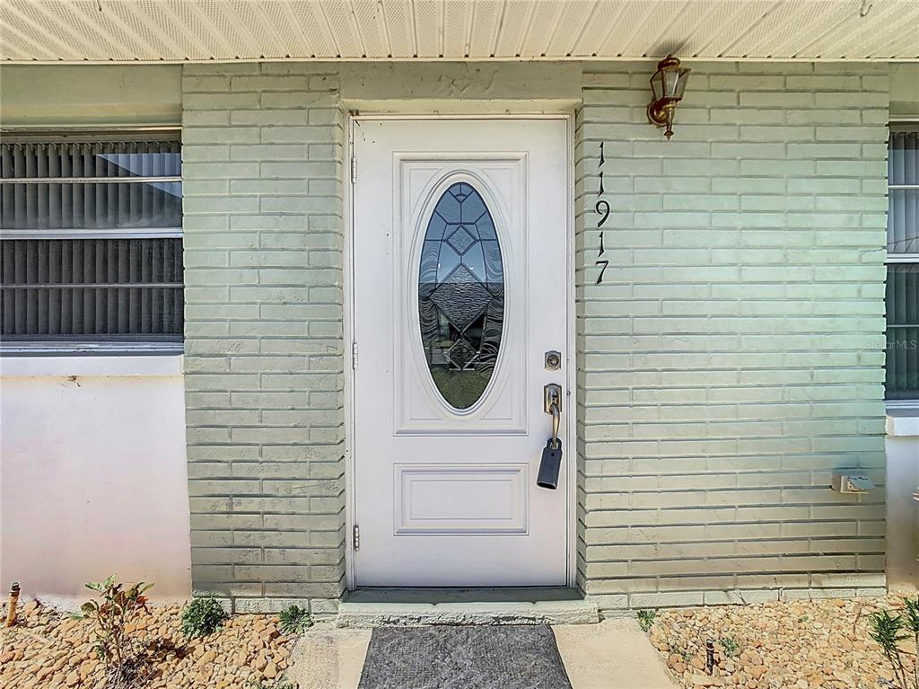 A white front door with an oval glass insert is set in a light green brick wall — 11917 BAYONET LANE UNIT 11917, NEW PORT RICHEY, FL