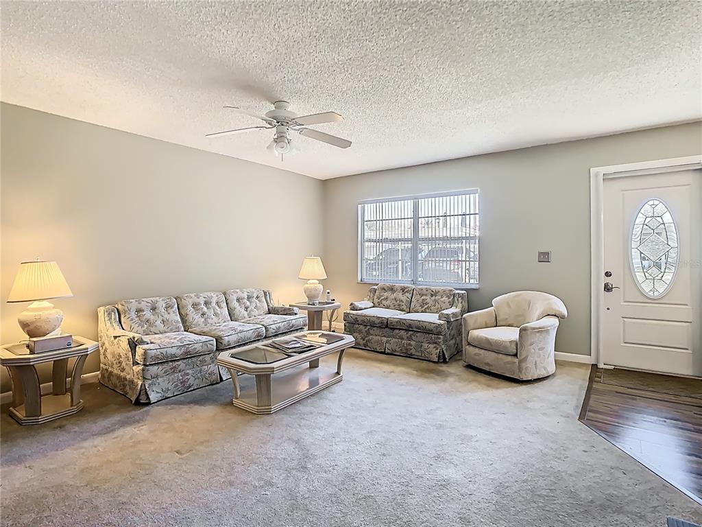 A living room features floral sofas, a glass-top coffee table, carpeted flooring, and a ceiling fan — 11917 BAYONET LANE UNIT 11917, NEW PORT RICHEY, FL