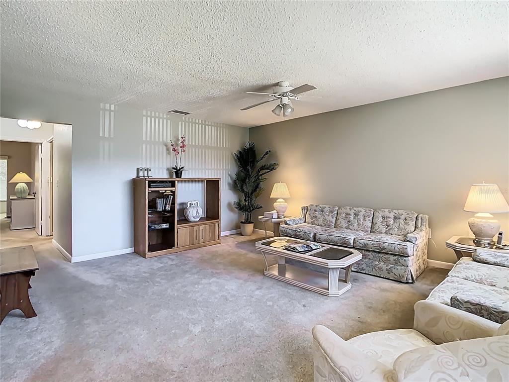 A living room features floral sofas, a wooden entertainment center, and a ceiling fan — 11917 BAYONET LANE UNIT 11917, NEW PORT RICHEY, FL