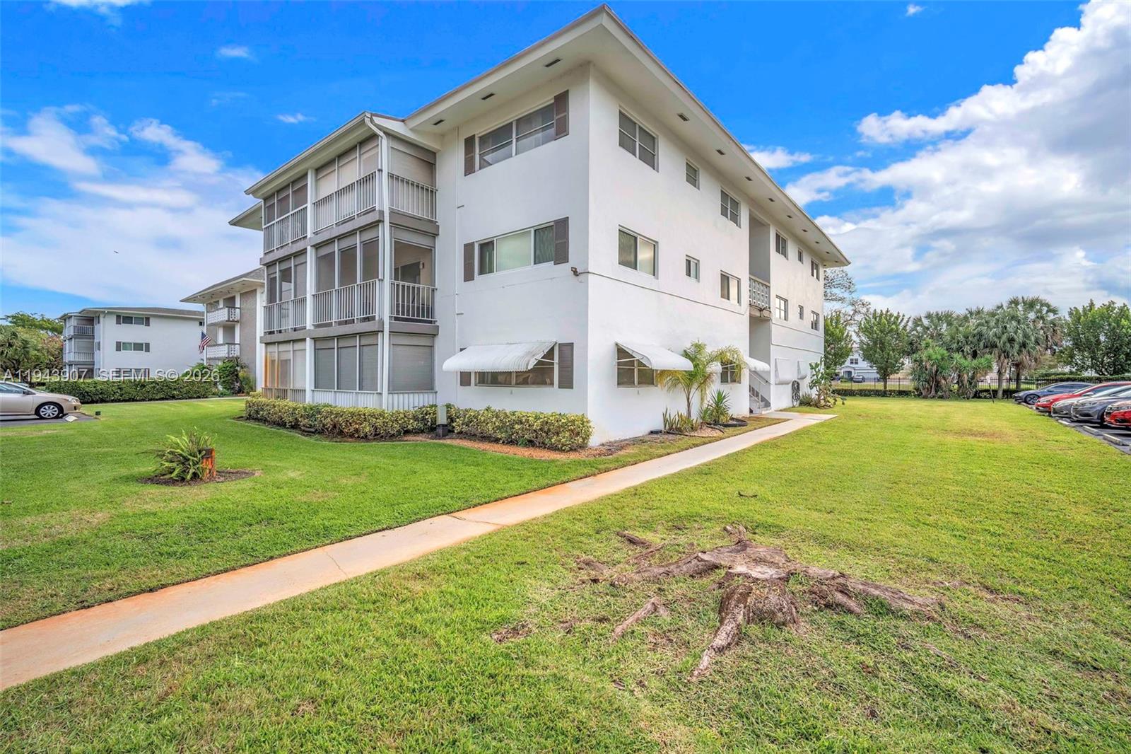 A three-story white apartment building features screened balconies and a sidewalk on a grassy lawn — 1201 Hillcrest Ct # 102, Hollywood FL 33021, HOLLYWOOD, FL