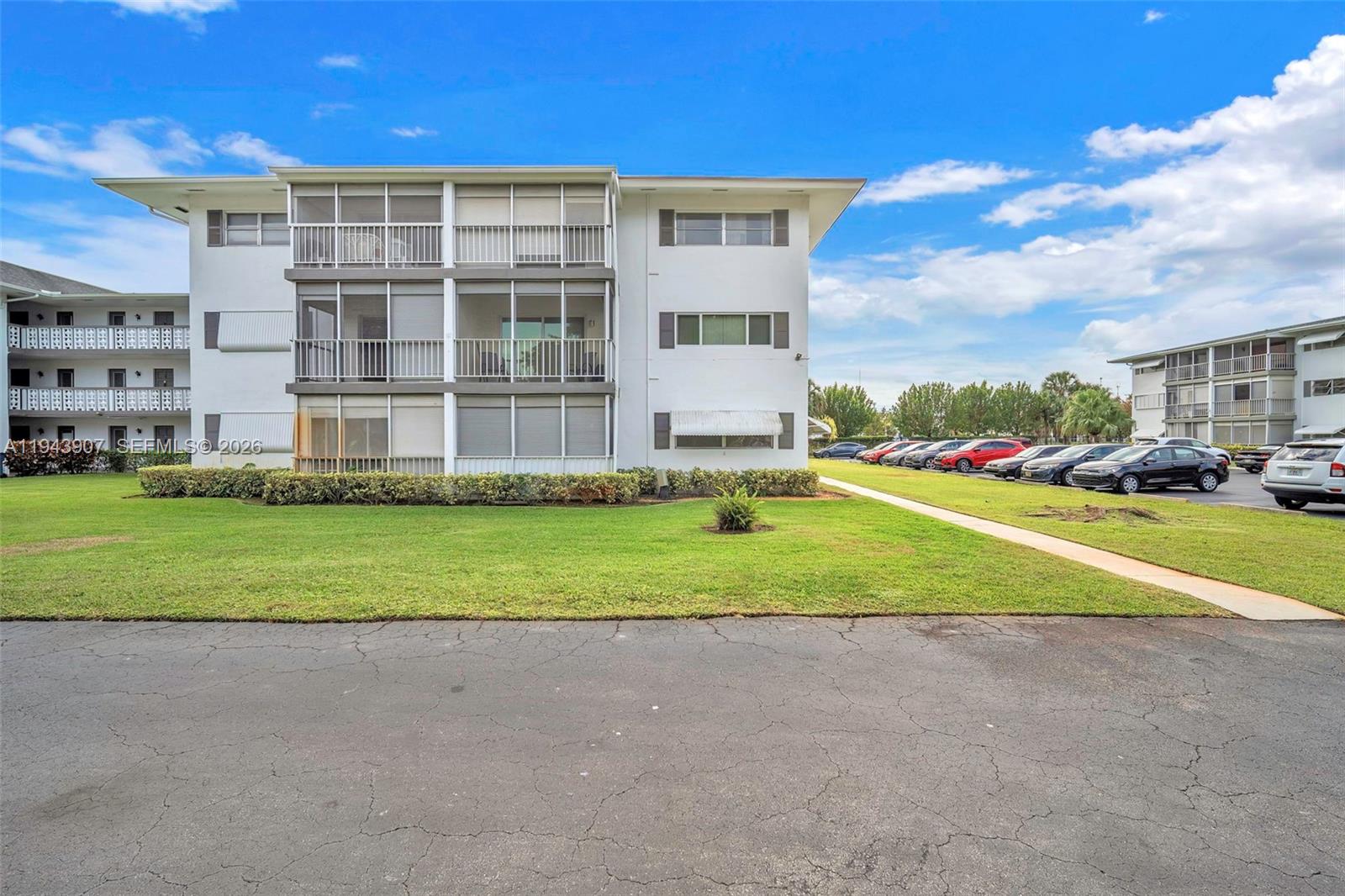 The exterior of a multi-story apartment building features screened balconies and a parking lot — 1201 Hillcrest Ct # 102, Hollywood FL 33021, HOLLYWOOD, FL