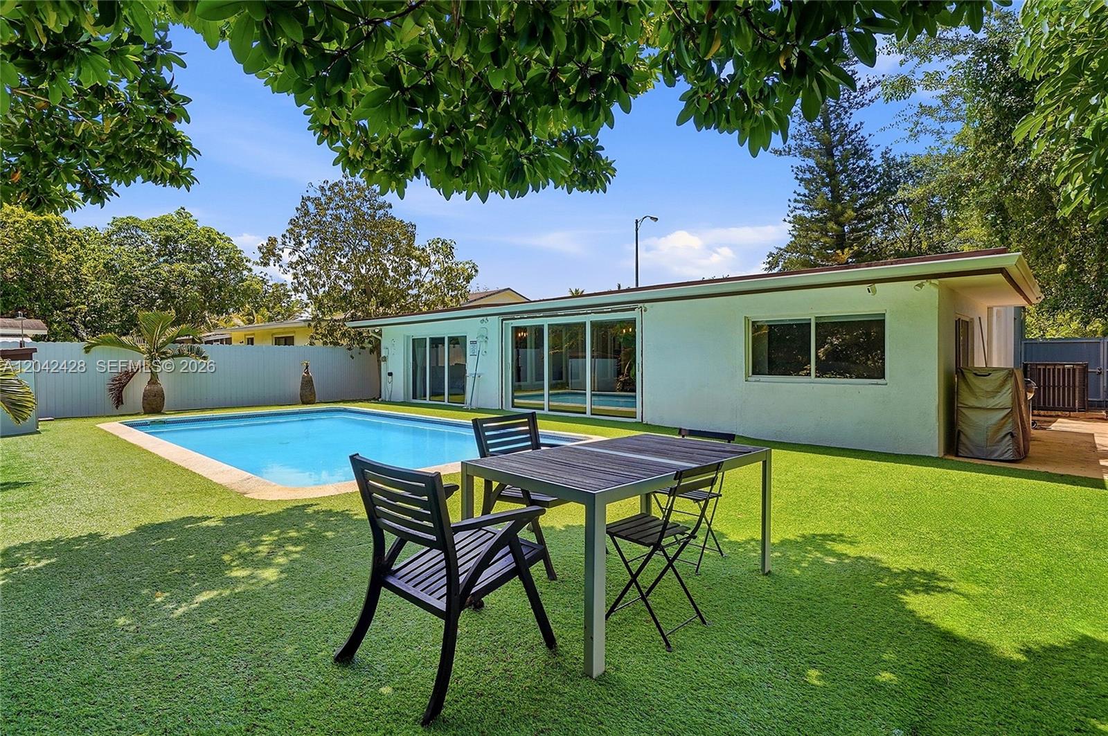 A backyard features a swimming pool, artificial turf, and a patio table with chairs — 110 NW 125th St, North Miami FL 33168, NORTH MIAMI, FL