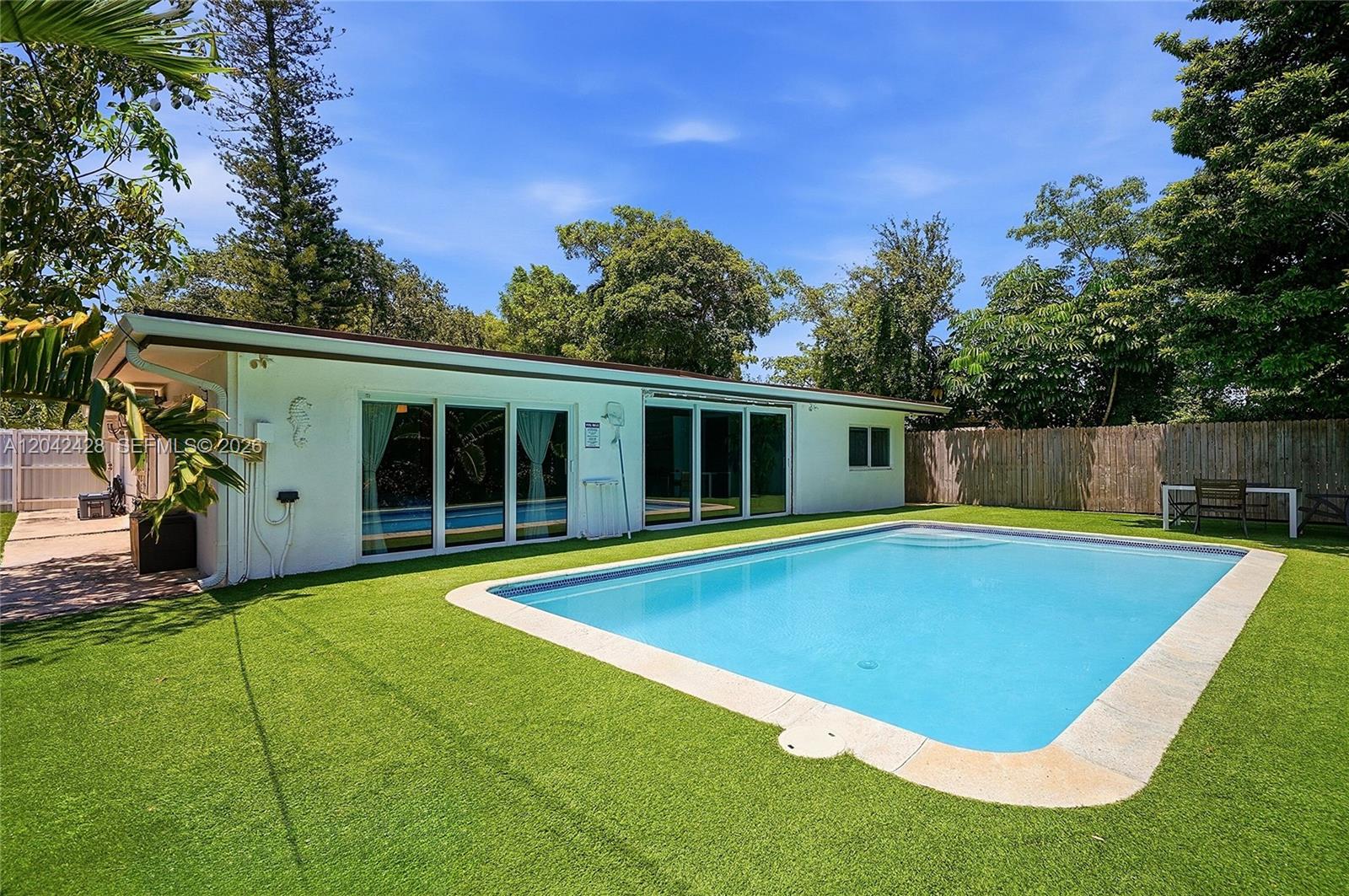 A white house with sliding glass doors overlooks a rectangular swimming pool and artificial lawn — 110 NW 125th St, North Miami FL 33168, NORTH MIAMI, FL