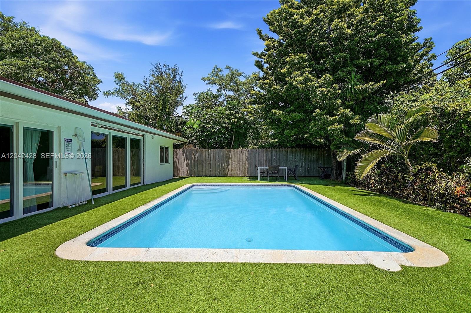 A rectangular swimming pool sits in a backyard with artificial turf and a wooden fence — 110 NW 125th St, North Miami FL 33168, NORTH MIAMI, FL