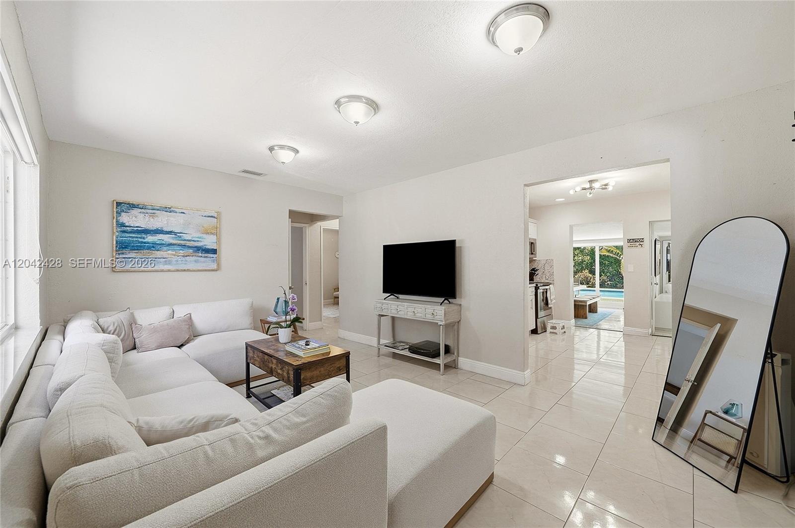 A living room features a white sectional sofa, a television on a console, and tile flooring — 110 NW 125th St, North Miami FL 33168, NORTH MIAMI, FL