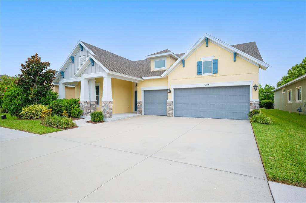 A yellow house with a three-car garage, stone accents, and a covered front porch — 6312 WAVES END PLACE, APOLLO BEACH, FL