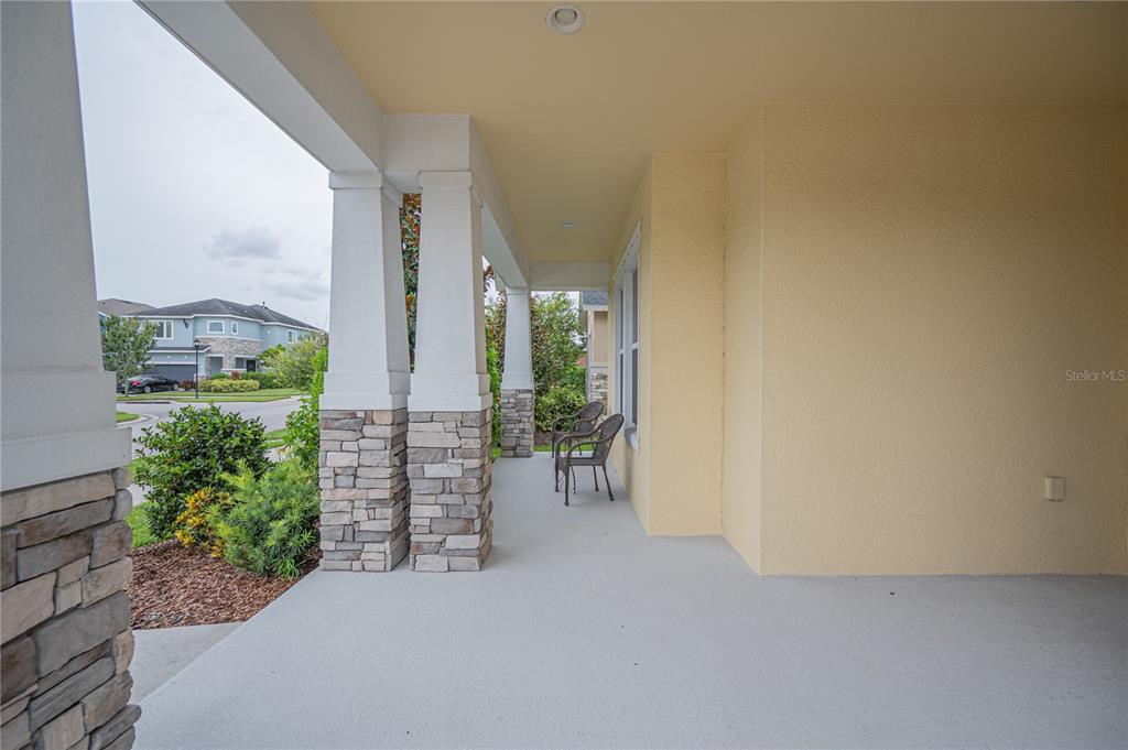 A covered front porch features stone-based columns, a concrete floor, and two outdoor chairs — 6312 WAVES END PLACE, APOLLO BEACH, FL
