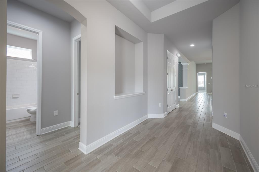 A hallway with light wood-look tile flooring leads past a recessed wall niche and bathroom — 6312 WAVES END PLACE, APOLLO BEACH, FL