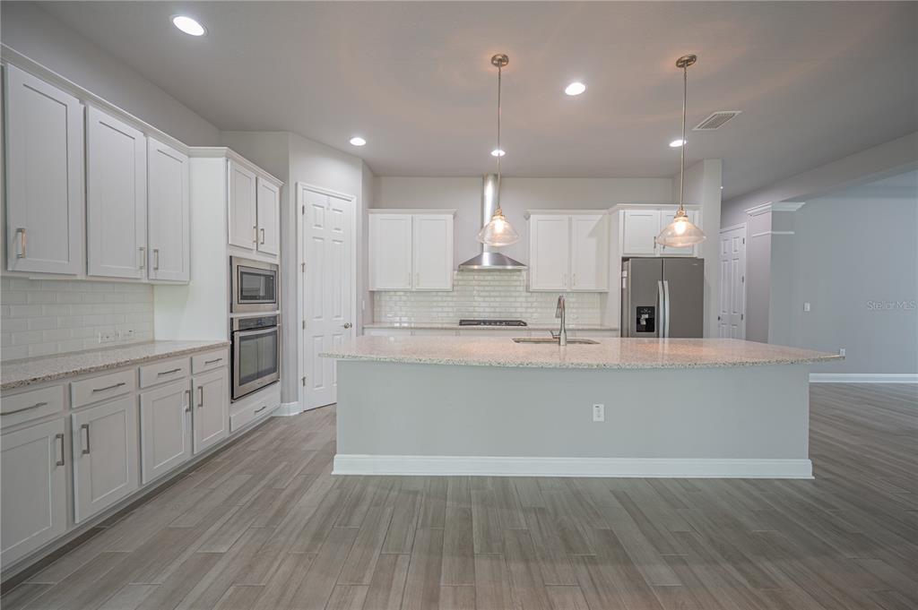 A modern kitchen features white cabinetry, granite countertops, stainless steel appliances, and wood-look tile flooring — 6312 WAVES END PLACE, APOLLO BEACH, FL