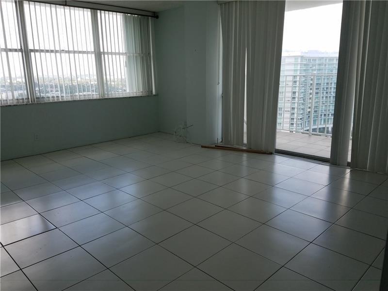 An empty room with light-colored tile flooring, large windows, and a balcony overlooking buildings — 111 Briny Avenue # 2011, Pompano Beach FL 33062, POMPANO BEACH, FL