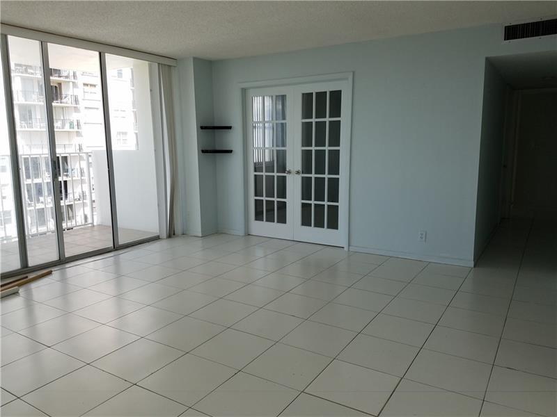 An empty room with white tile floors, a sliding glass door, and white French doors — 111 Briny Avenue # 2011, Pompano Beach FL 33062, POMPANO BEACH, FL