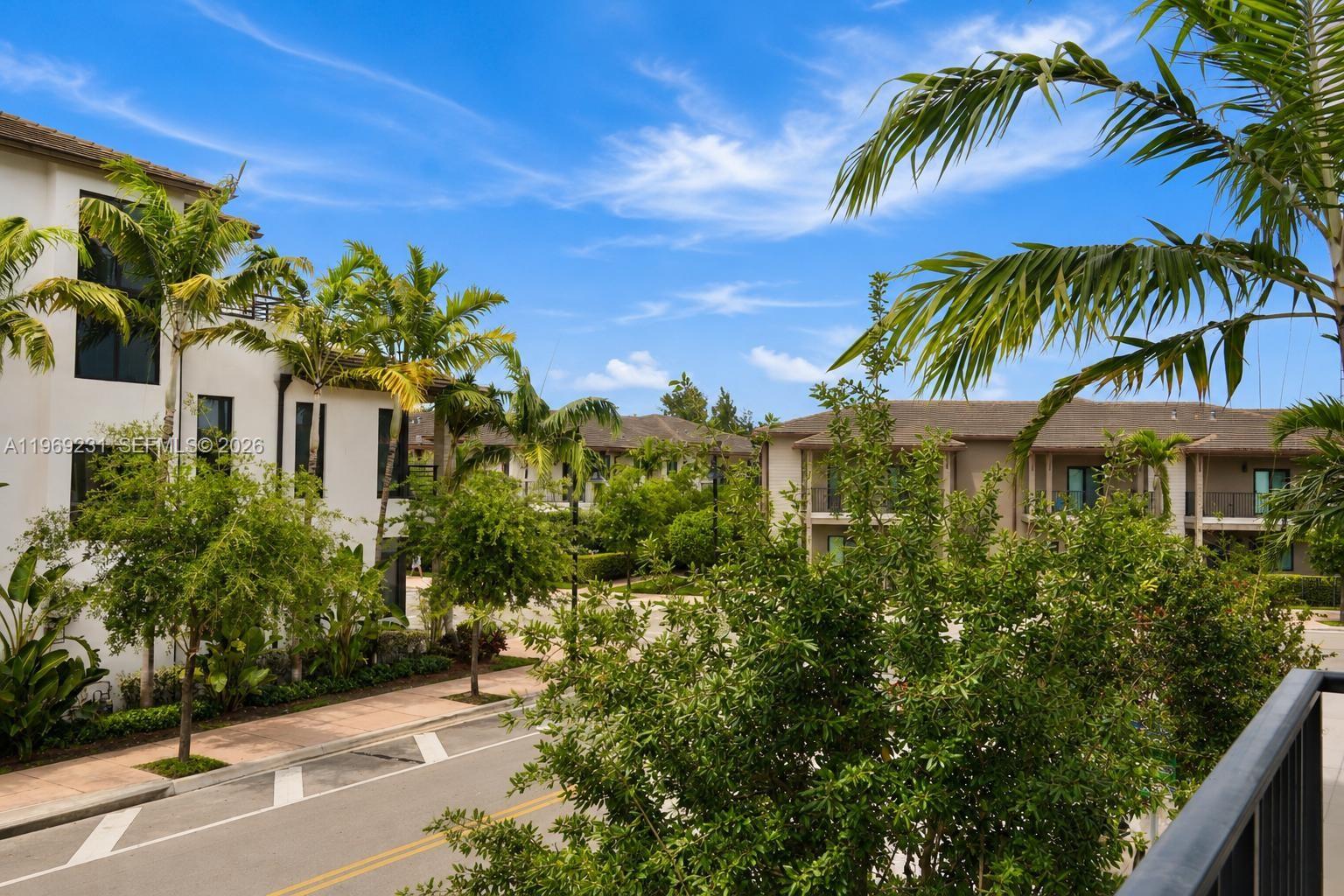 An exterior view of a residential street lined with multi-story buildings and palm trees — 4745 NW 84th Ct # 14, Doral FL 33166, DORAL, FL