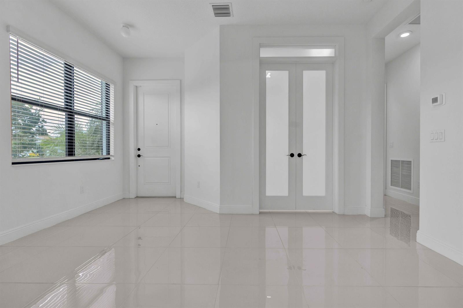 An empty room with white walls, light tile flooring, a window, and two sets of doors — 5501 Santa Rosa Lane, Westlake FL 33470, WESTLAKE, FL