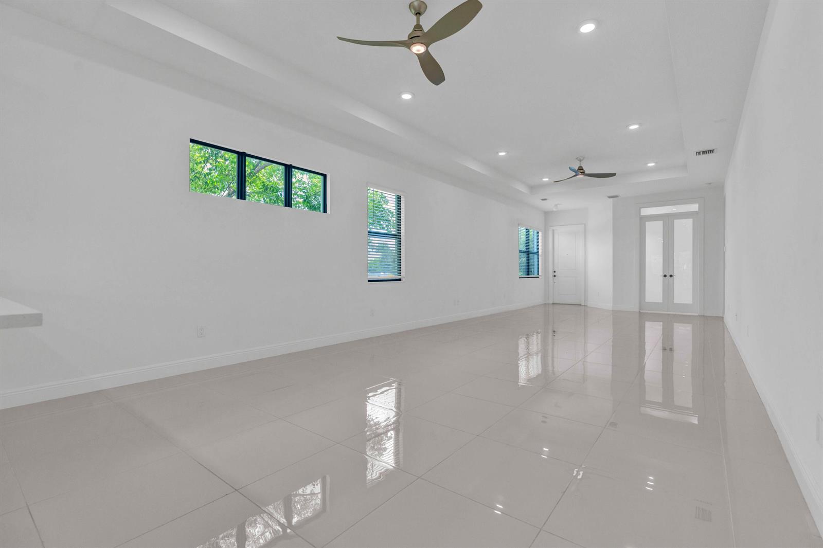 An empty, white-walled room features glossy tile flooring, two ceiling fans, and several windows — 5501 Santa Rosa Lane, Westlake FL 33470, WESTLAKE, FL