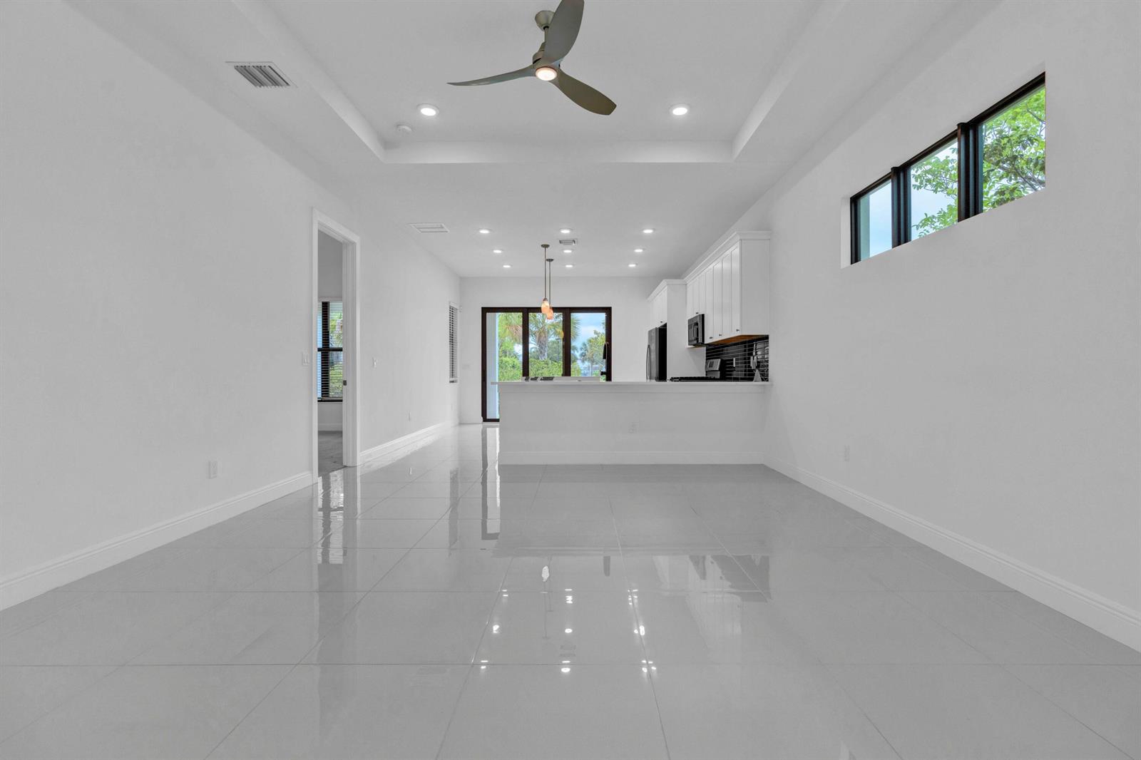 A bright, open-concept living area features white walls, glossy tile floors, and a modern kitchen — 5501 Santa Rosa Lane, Westlake FL 33470, WESTLAKE, FL